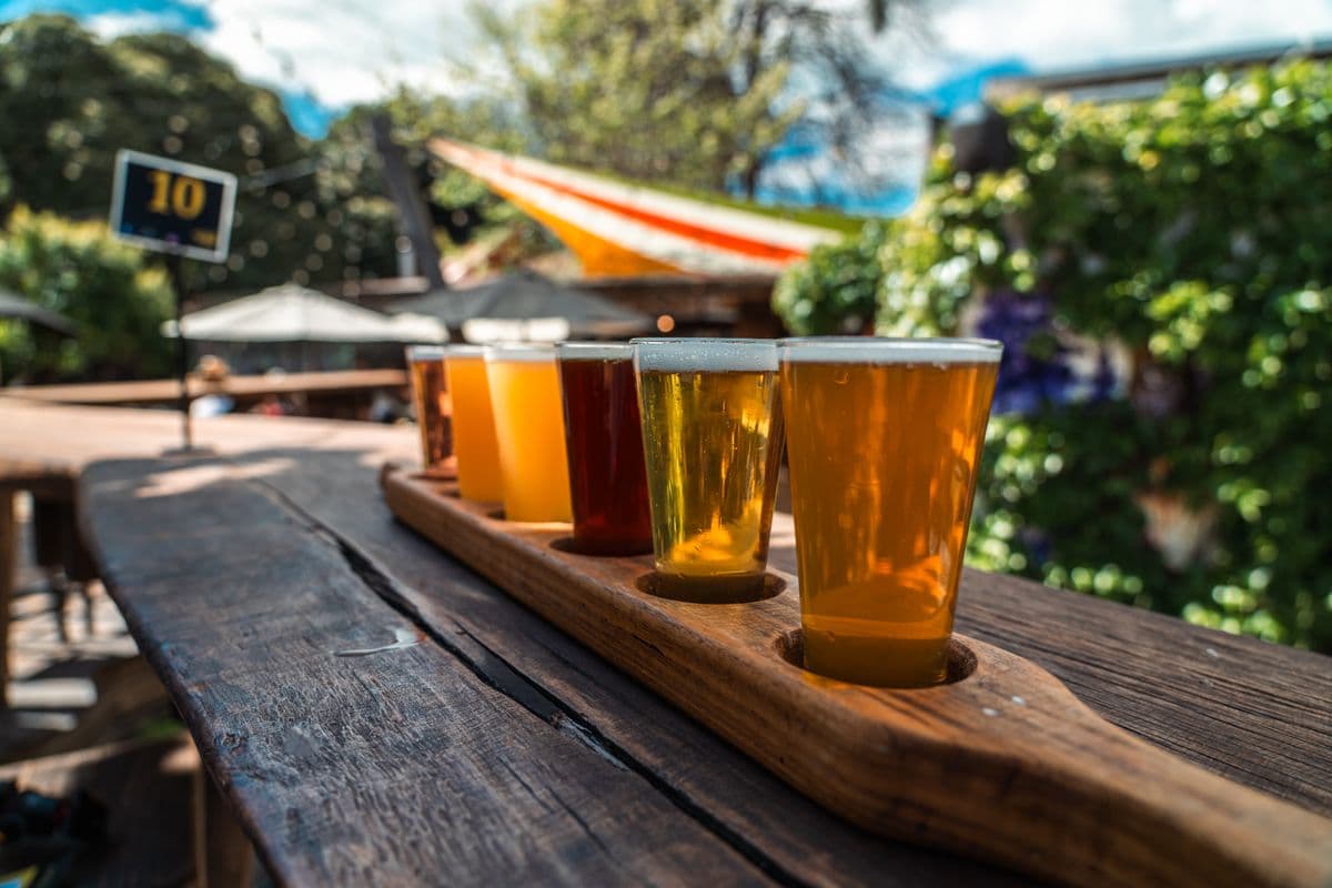 A tasting flight of craft beers on a wooden tray outdoors