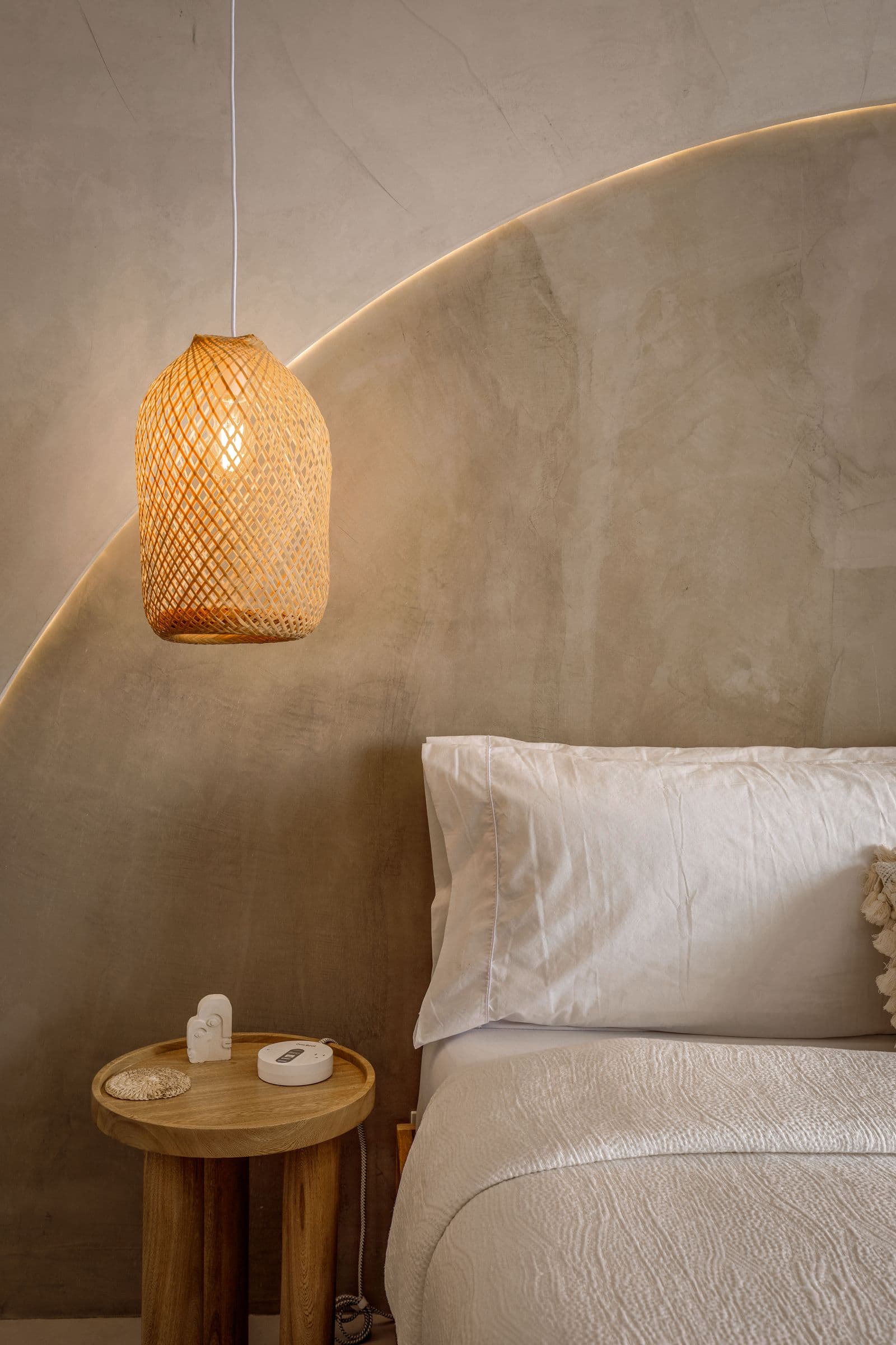 A calm bedroom with white linen and a woven pendant light